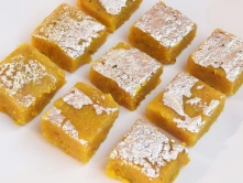 Best Indian Moong Dhal Burfi Sweets Products in Chennai A decorative plate holds yellow cake squares of moong-dal-burfi, displayed with powdered sugar.